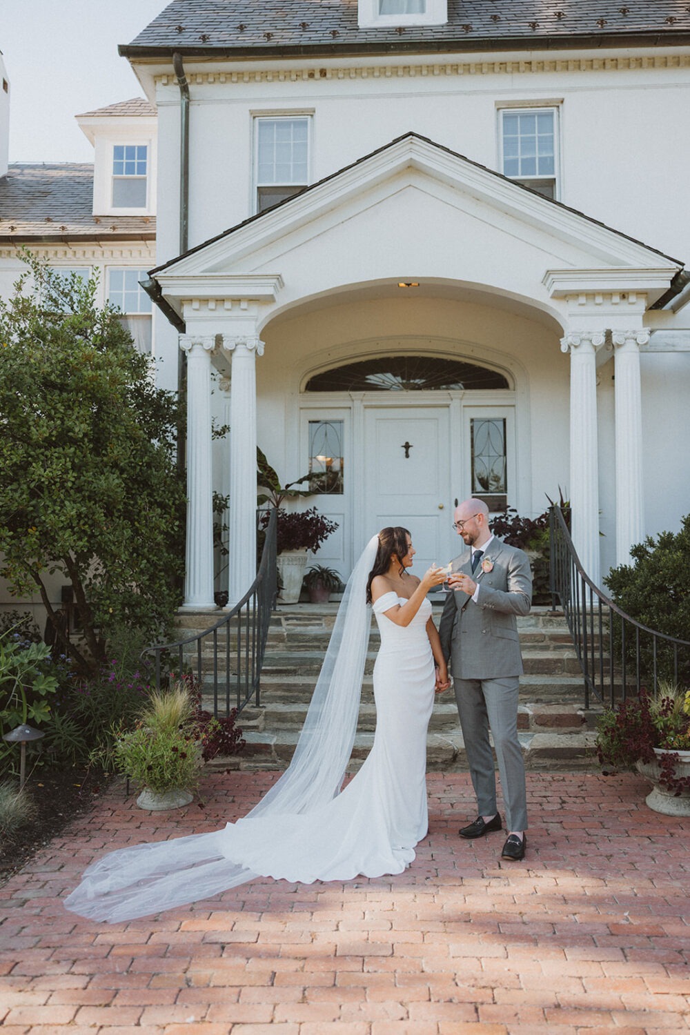 couple toast with their cocktail drinks in front of white building at River Farm Alexandria Virginia
