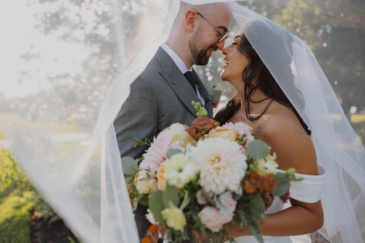 couple smiling together underneath veil and holding wedding flowers